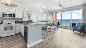 A modern kitchen with white cabinets, a microwave, and a stove. There is a dining area with a white table and chairs, and a balcony with a view of the ocean. - Oceanfront, Swimming Pool, 14th Floor Condo (Panama City Beach)