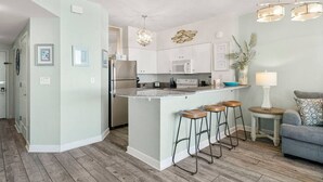 A modern kitchen with a central island, bar stools, a refrigerator, and a microwave. - Oceanfront, Swimming Pool, 14th Floor Condo (Panama City Beach)