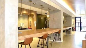 A modern kitchen with a long counter, bar stools, pendant lights, and a visible refrigerator.