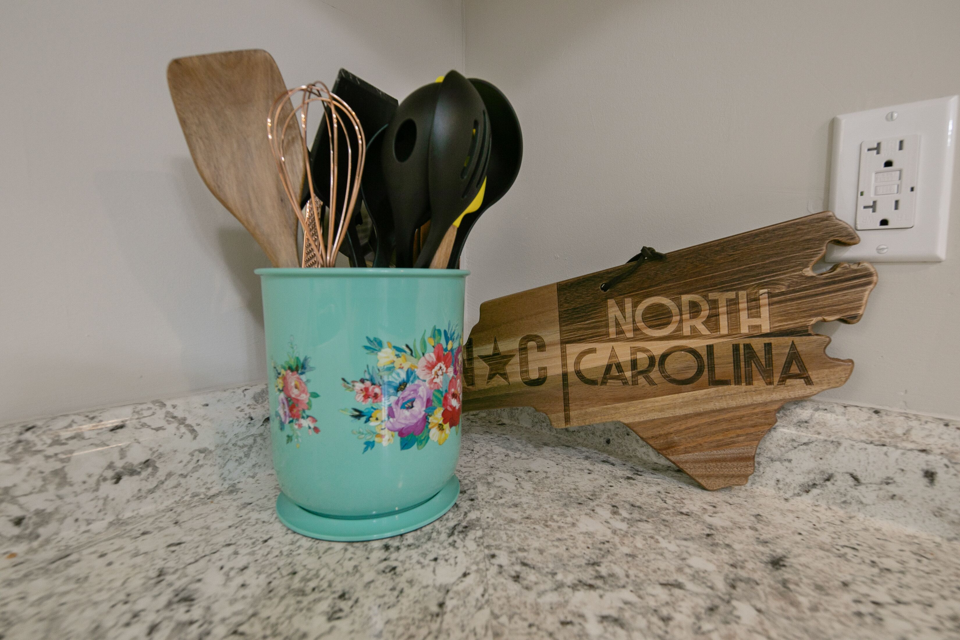 Un comptoir de cuisine avec un porte-ustensiles de couleur turquoise et un panneau en bois en forme de l’État de Caroline du Nord.