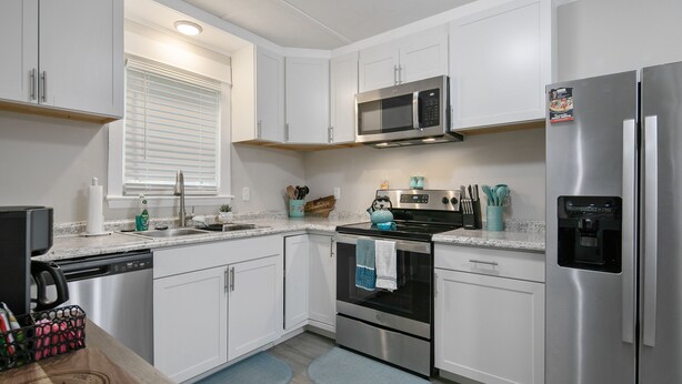 A modern kitchen with white cabinets, stainless steel appliances, a microwave, and a refrigerator. - Your Newest, Remodeled, and Fully-Furnished AirB&B in the Heart of Fayetteville! (Fayetteville)