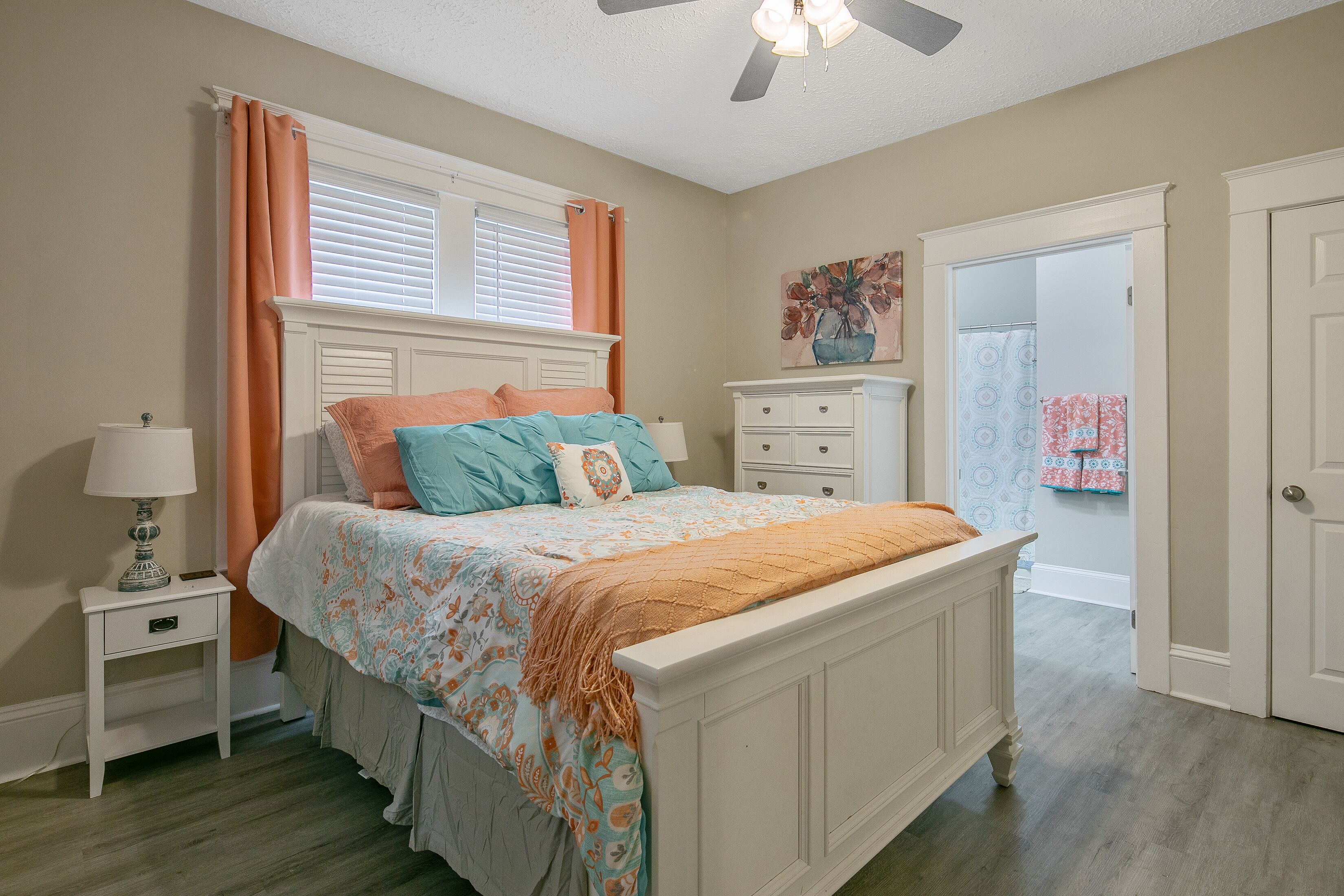 A bedroom with a bed, nightstand, dresser, and a door leading to another room.