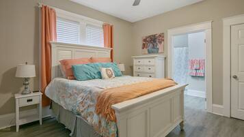 A bedroom with a bed, nightstand, dresser, and a door leading to another room.