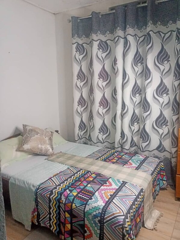 A bedroom with a bed, pillows, a patterned bedspread, and curtains. - PagersHome Suites - RUSTIC (Kigali)