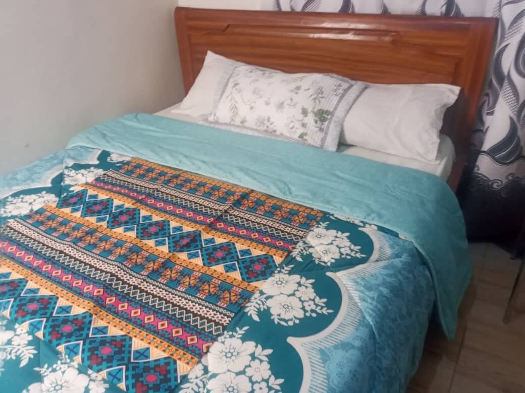 Una cama con colcha estampada, cabecera de madera y dos almohadas.