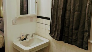 Ein Badezimmer mit einem weißen Waschbecken, einem Spiegel, zwei Wandleuchten, einem Handtuchhalter und einer Duschvorhang.