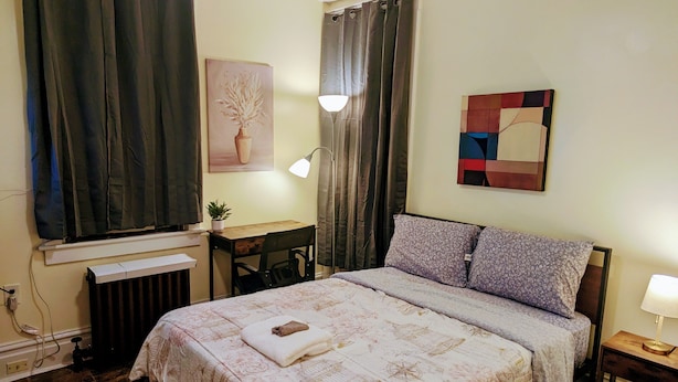 Ein Schlafzimmer mit einem Bett, einem Schreibtisch, einem Stuhl, einer Lampe und einem Bild an der Wand.