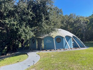 A unique, dome-shaped structure with a pathway leading to it, surrounded by lush greenery. - UFO Dome Getaway with Arcade Loft, Fire Pit & Retro Fun in Lake Placid, Florida (Lake Placid)