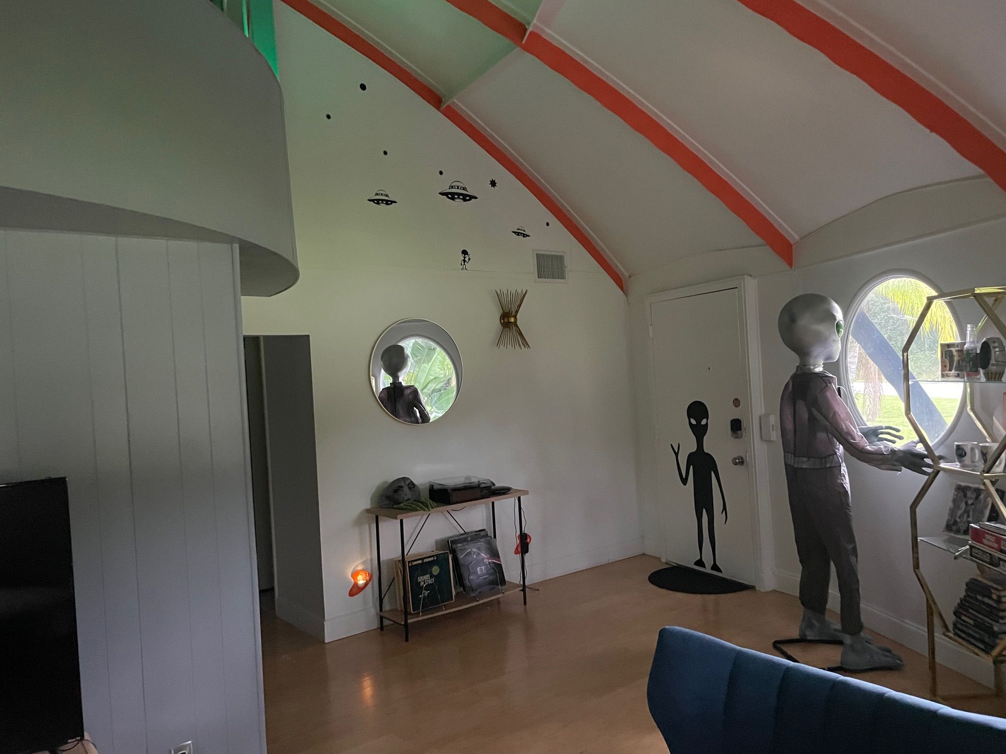 A room with a high ceiling, a round mirror, a shelf with books, and a mannequin.