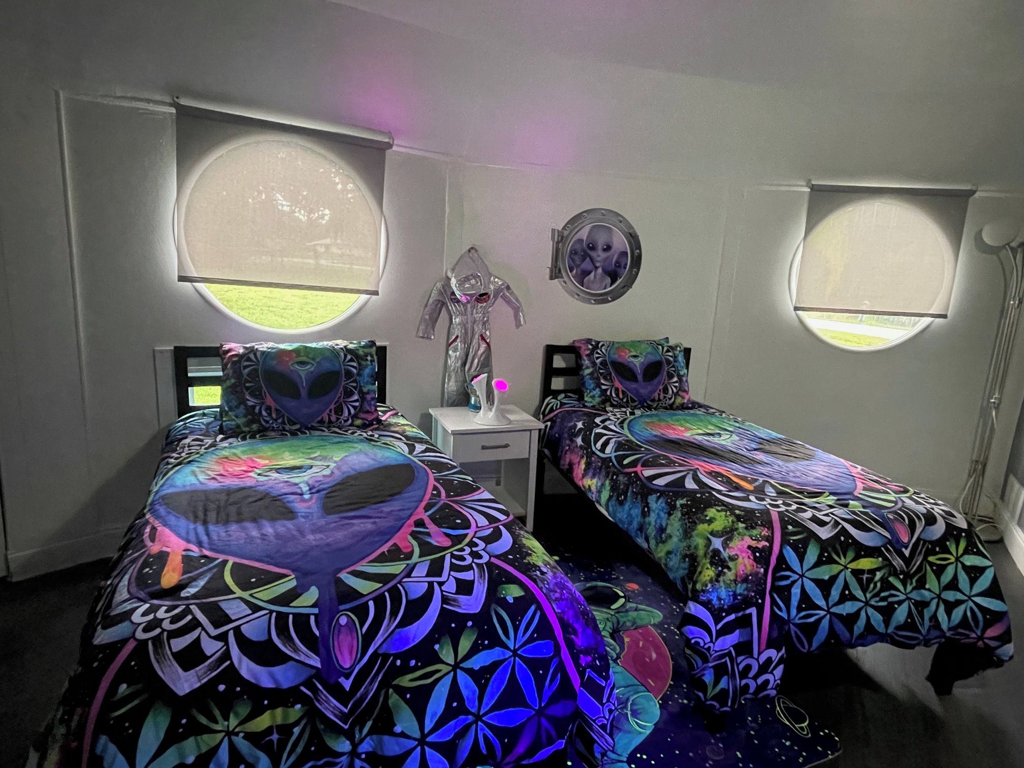 A bedroom with two beds, each with a unique geometric-patterned bedspread, a small bedside table, and a wall-mounted mirror.