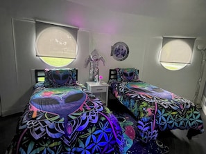 A bedroom with two beds, each with a unique geometric-patterned bedspread, a small bedside table, and a wall-mounted mirror. - UFO Dome Getaway with Arcade Loft, Fire Pit & Retro Fun in Lake Placid, Florida (Lake Placid)