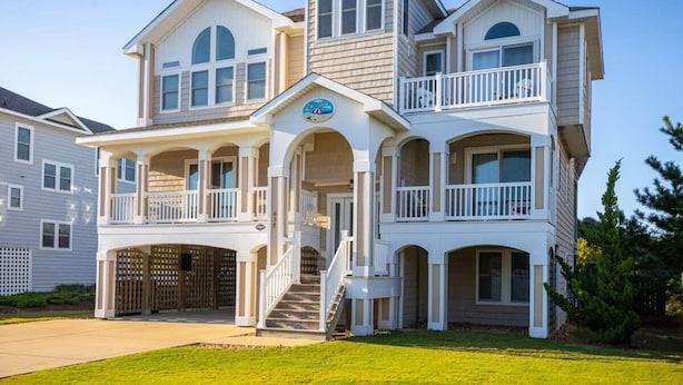 A two-story house with a balcony, a garage, and a well-maintained lawn. - 3min Walk to Beach, Pool, Hot Tub, & Game Room! (Corolla)