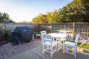 An outdoor patio with a barbecue grill, white plastic chairs, and a table. - 3min Walk to Beach, Pool, Hot Tub, & Game Room! (Corolla)