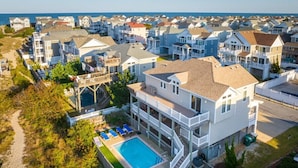 A beachfront property with a large swimming pool, multiple balconies, and a view of the ocean. - 3min Walk to Beach, Pool, Hot Tub, & Game Room! (Corolla)