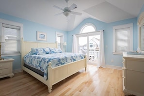 Un dormitorio con cama, ventilador de techo, cómoda y ventana con persianas.