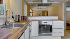 Et moderne køkken med vask i rustfrit stål, indbygget ovn og træbordplade.