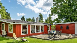 Et rødt hus med terrasse, grill og swimmingpool.