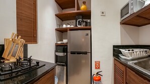 A compact kitchen with a stove, refrigerator, and microwave. - Frangipani Villa Kuning At Berawa (Canggu)