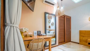 A modern room with a wooden desk, a wicker chair, a bed with a headboard, and a large mirror. - Frangipani Villa Kuning At Berawa (Canggu)