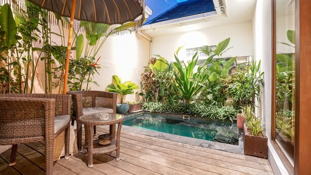 A wooden deck with wicker furniture, a pool, and lush tropical plants. - Frangipani Villa Kuning At Berawa (Canggu)