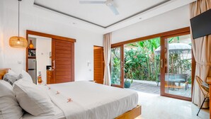 A modern bedroom with a large bed, a ceiling fan, and a sliding glass door leading to a patio with plants and furniture. - Frangipani Villa Kuning At Berawa (Canggu)