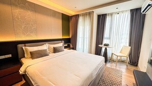 A hotel room with a large bed, a bedside table, a chair, and a small table. - Cha Chiangmai Luxury (Chiang Mai)