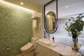 Um banheiro com parede de azulejos hexagonais, vaso sanitário, pia com bancada de mármore, espelho e planta em vaso.