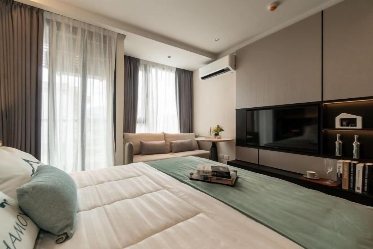 A modern hotel room with a large bed, a sofa, a TV, and a small table with a plant.