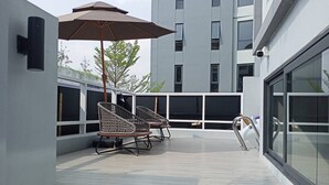 A modern outdoor seating area with two wicker chairs and a large umbrella, overlooking a cityscape. - Cha Chiangmai Luxury (Chiang Mai)