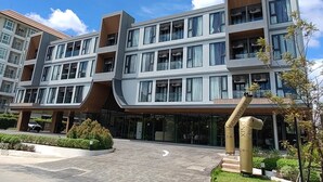 A modern multi-story building with a curved facade, large windows, and a central entrance area with a landscaped garden. - Cha Chiangmai Luxury (Chiang Mai)