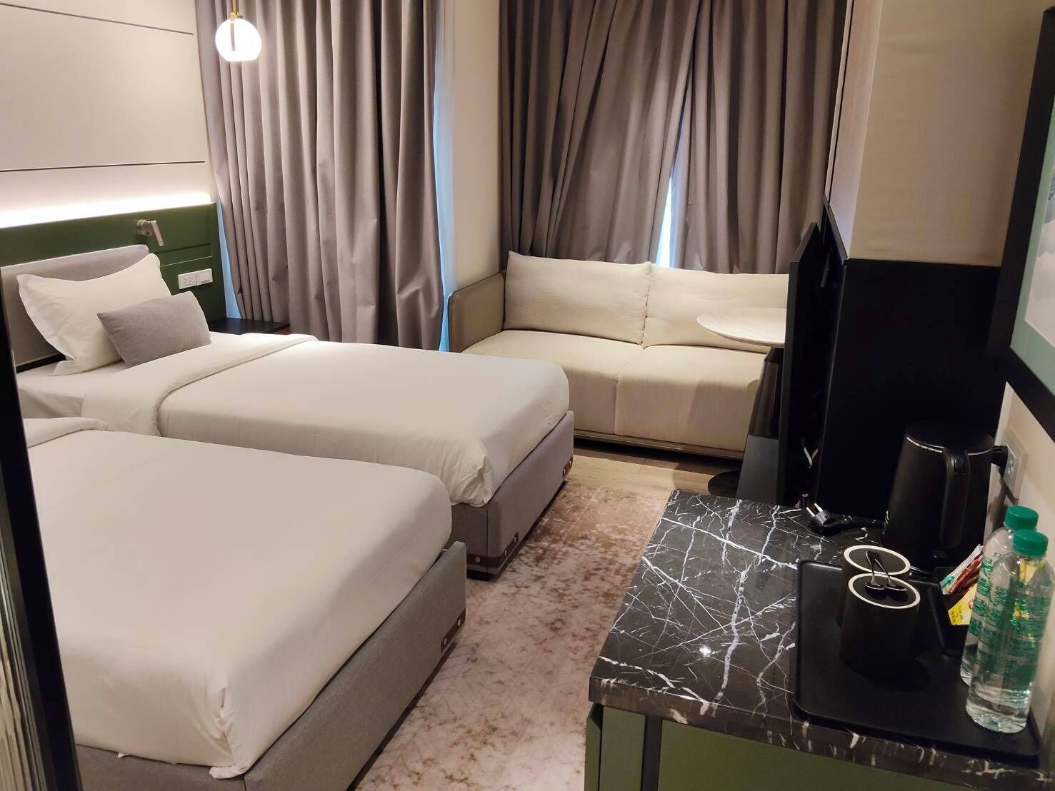 A hotel room with two beds, a sofa, a small table, a TV, and a minibar.