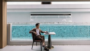 A man sitting at a table by a pool with a view of a waterfall. - Cha Chiangmai Luxury (Chiang Mai)