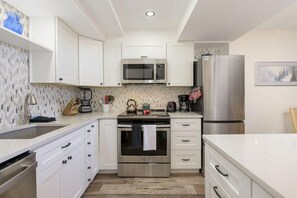 Uma cozinha moderna com armários brancos, eletrodomésticos de aço inoxidável e painel de azulejos.