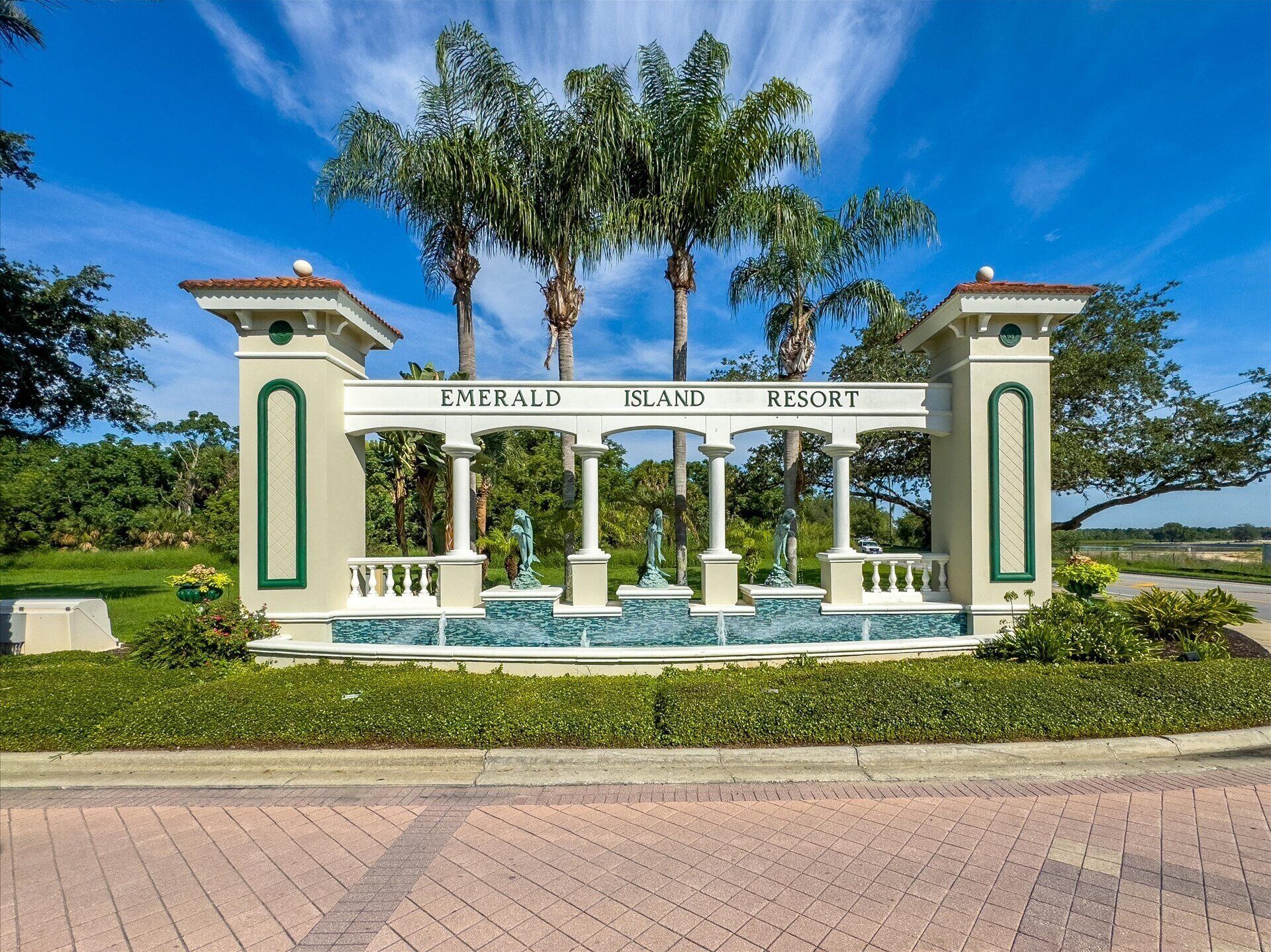 A sign for Emerald Island Resort with a classical architectural design, featuring columns and statues, surrounded by lush greenery and palm trees.