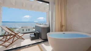 A balcony with a view of the sea, a hot tub, and a seating area with a table and chairs.