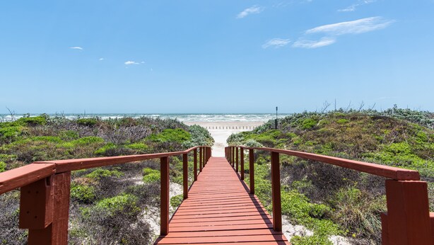 Un paseo marítimo de madera que lleva a una playa con cielo despejado.