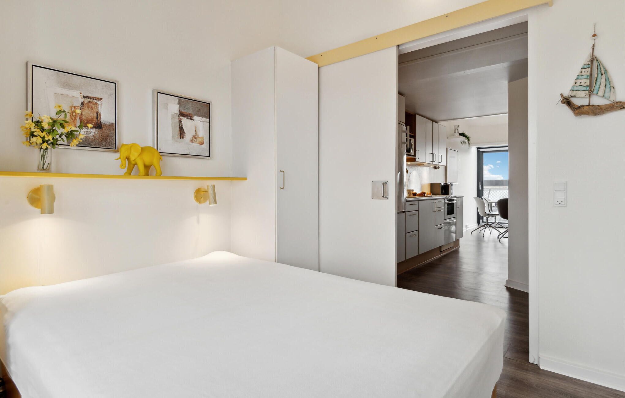Et moderne soveværelse med en seng, et lille skrivebord og udsigt til køkken og balkon.