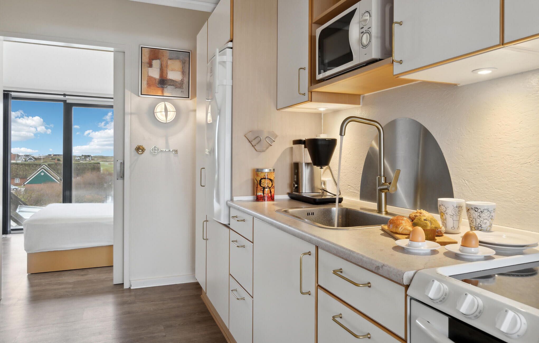 Eine moderne Küche mit Backofen, Mikrowelle und Kaffeemaschine. Es gibt ein Spülbecken mit Wasserhahn und ein Fenster mit Blick ins Grüne.
