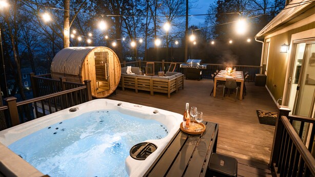 Ein Whirlpool auf einer Holzterrasse mit Lichterketten, eine Sauna und ein Essbereich mit Tisch für zwei Personen.