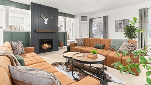 Ein modernes Wohnzimmer mit Kamin, einer großen Couch, einem Couchtisch und einem Deckenventilator.