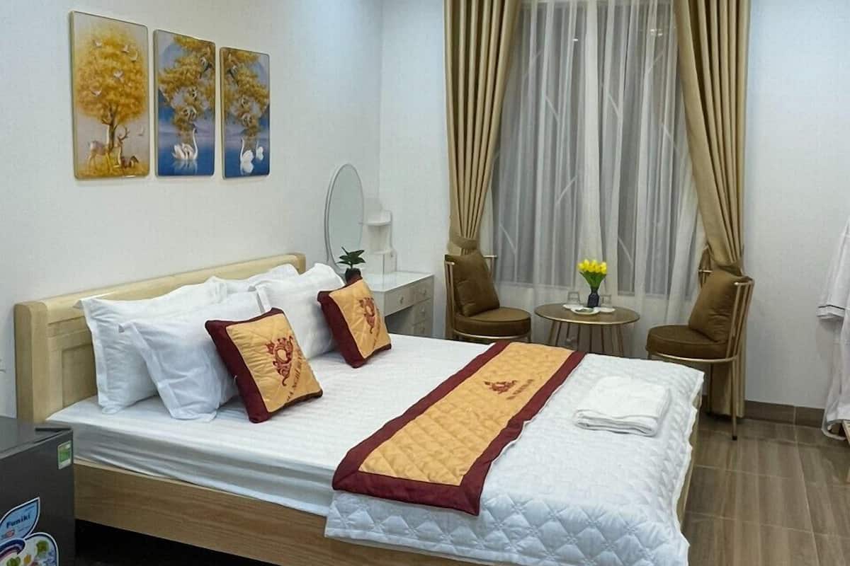 Quarto de hotel com uma cama, uma escrivaninha, uma cadeira, uma mesinha de centro com uma planta e uma janela com cortinas.