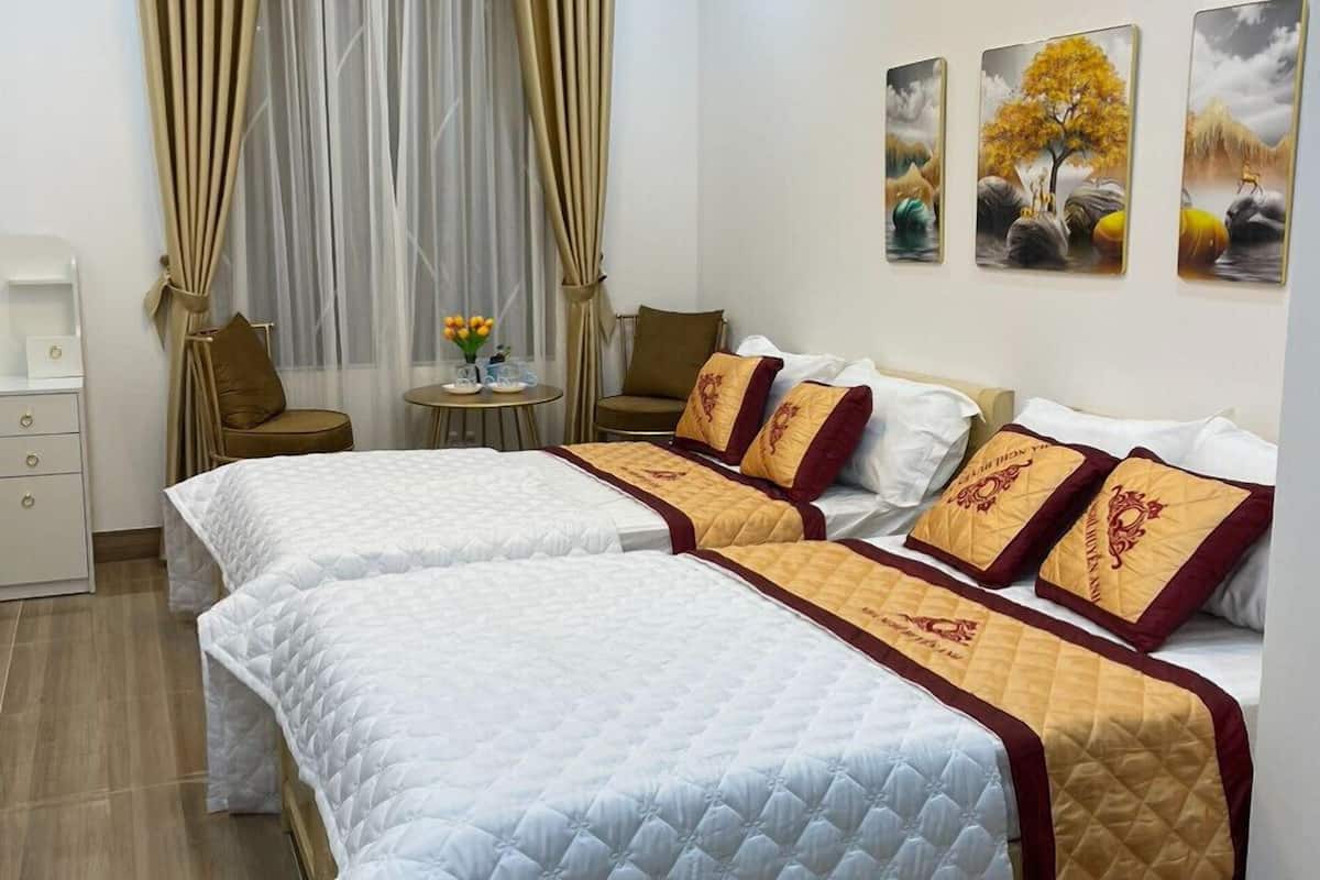Quarto de hotel com duas camas, uma mesinha com um vaso e três quadros na parede.