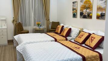 A hotel room with two beds, a small table, a chair, and artwork on the wall.
