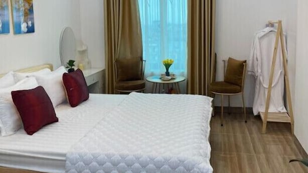 A hotel room with a bed, a chair, a table, a hanging coat rack, and a window with curtains. - Huyen Anh Hotel (Hanoi)