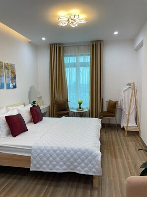 A hotel room with a bed, a chair, a table, a hanging coat rack, and a window with curtains. - Huyen Anh Hotel (Hanoi)