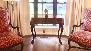 Ein Zimmer mit zwei roten, gemusterten Stühlen, einem Holztisch, einer Lampe und einem Fenster mit Vorhängen.