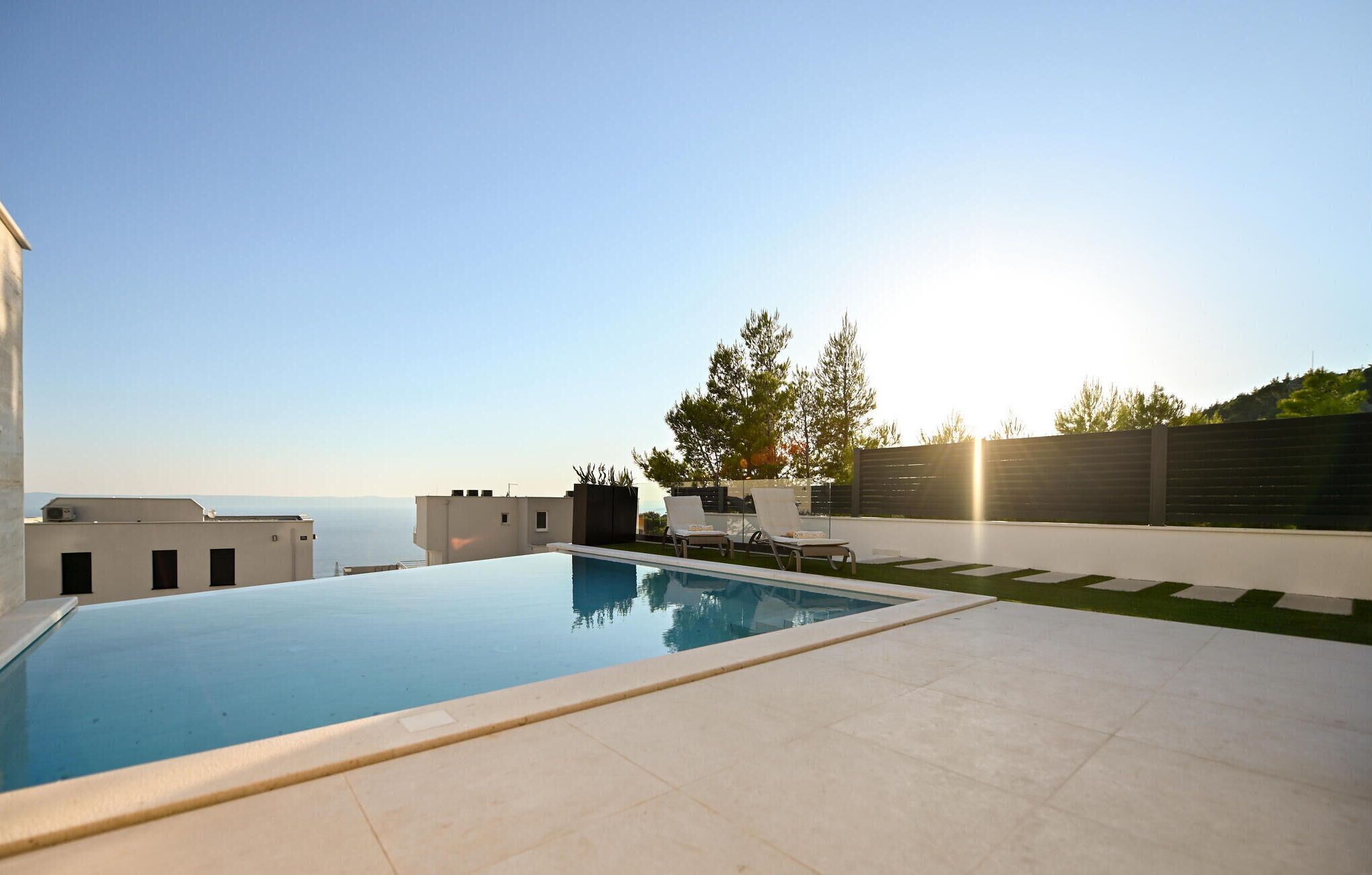 Una piscina moderna al aire libre con vistas despejadas al mar y una zona de césped con sillones de descanso.