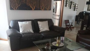 A living room with a black leather sofa, a glass coffee table, and a painting on the wall. - Edificio san thelmo laureles  (Medellín)
