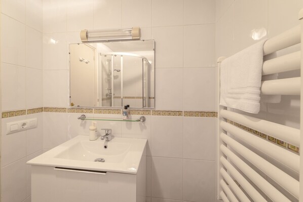 Un baño con lavamanos blanco, espejo y toallero.