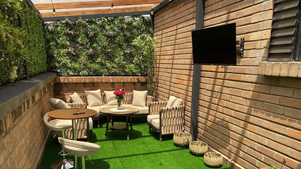Eine Terrasse mit einer Ziegelwand, künstlichem grünen Rasen, einer Sofagarnitur, einem runden Tisch und einem Topfpflanzen.